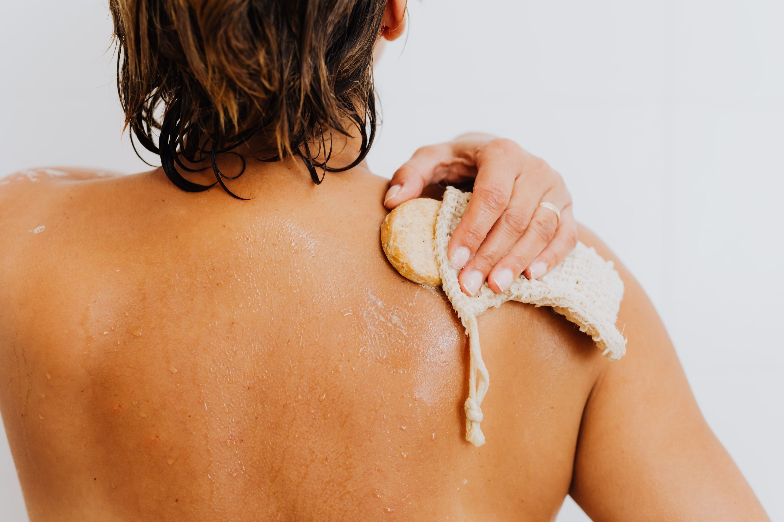 Personne exfoliant son épaule avec une fleur de bain