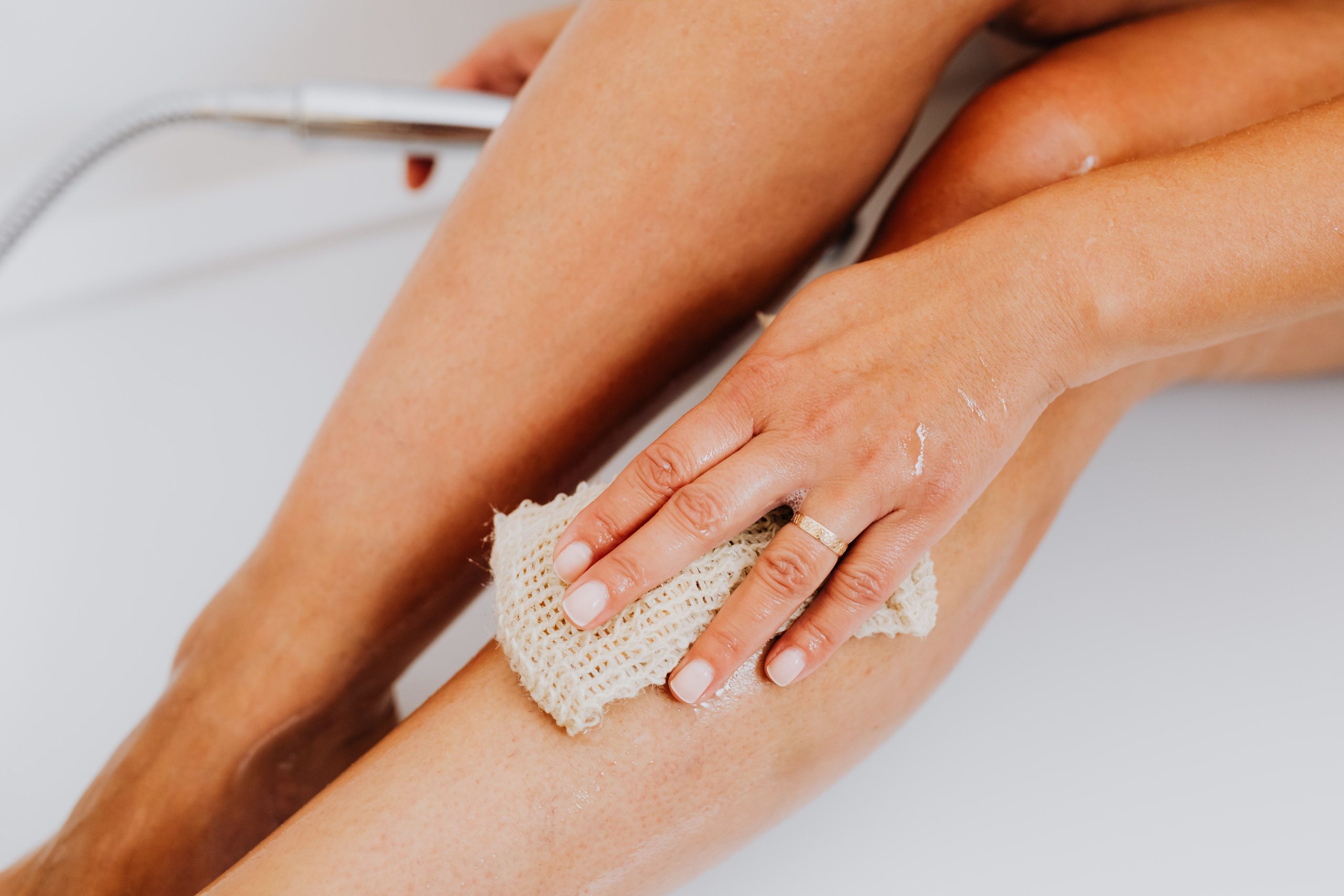 Main gommant une jambe avec loofah naturel