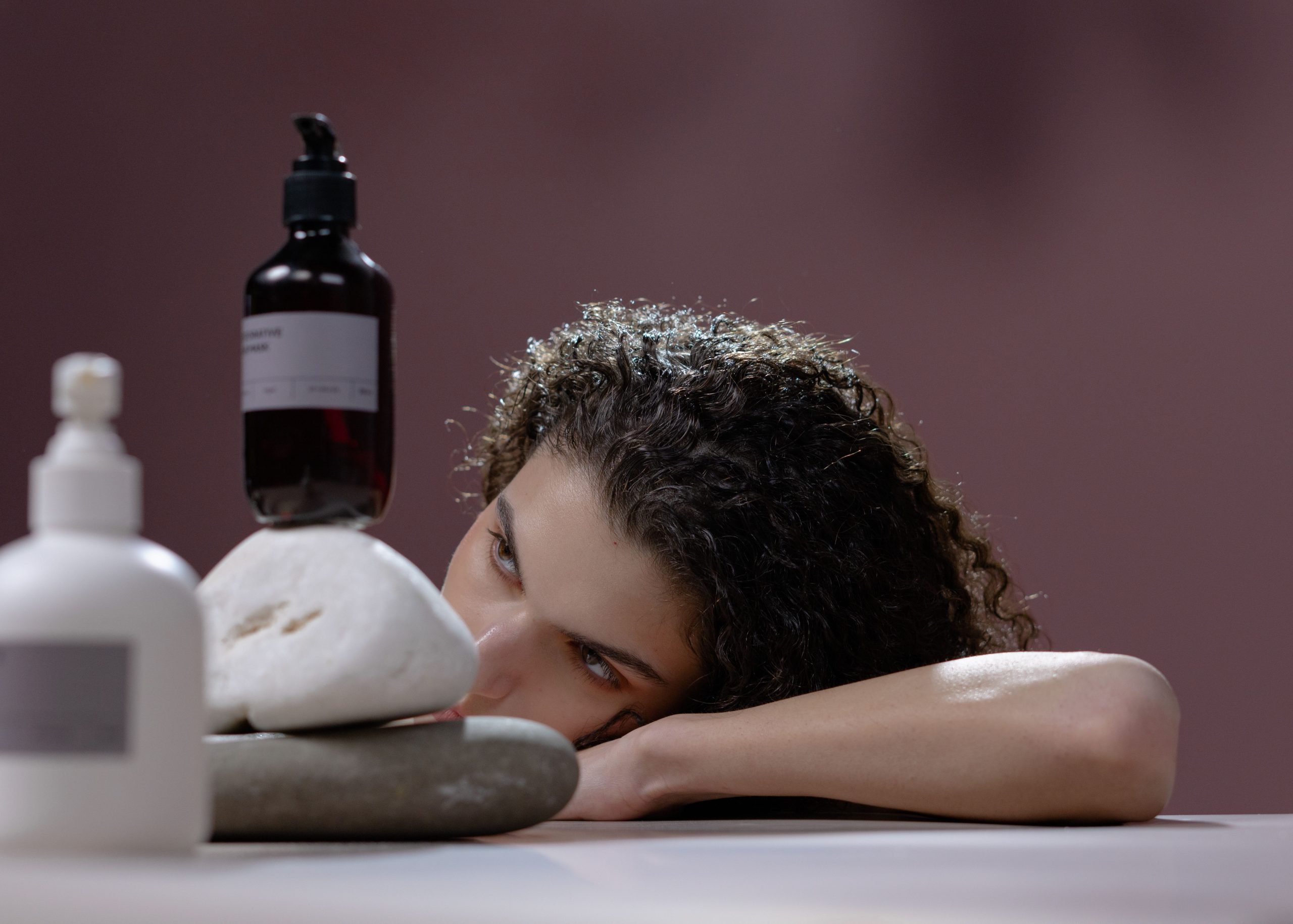 Femme cheveux boucles tenant bouteilles cosmétiques